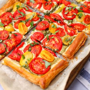 A vegan tomato tart made with puff pastry cut into pieces on a baking sheet.