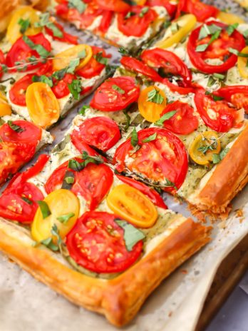 A vegan tomato tart made with puff pastry cut into pieces on a baking sheet.