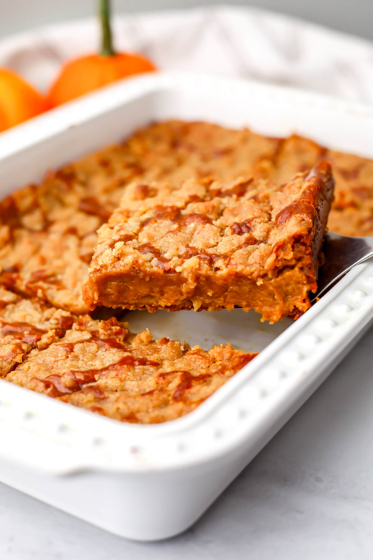 A slice of pumpkin pie cake being taken out of a white baking pan.
