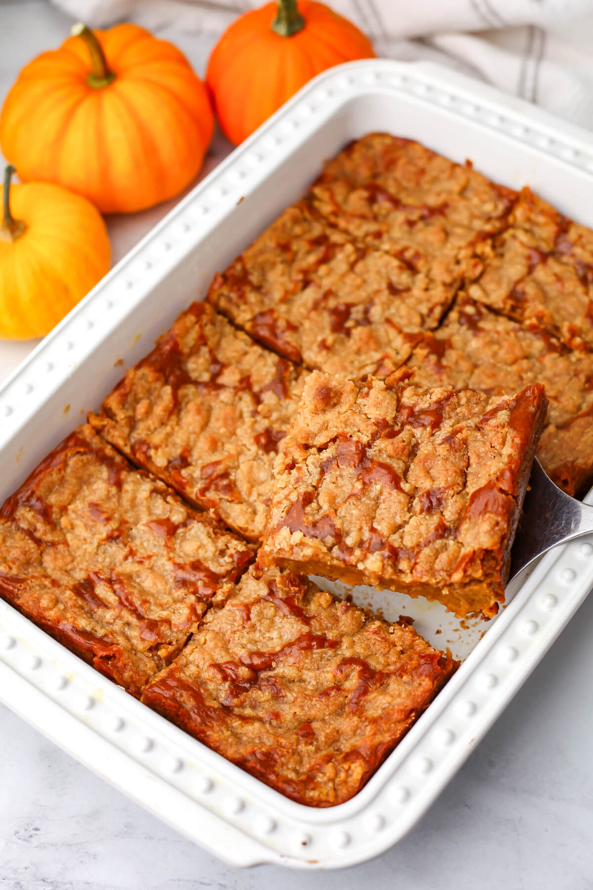 A vegan pumpkin pie cake in a white baking dish with someone taking a piece out of it.