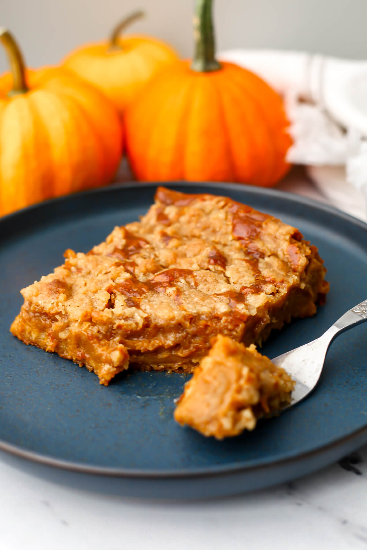 A piece of pumpkin pie cake on a blue plate with little pumpkins behind it.
