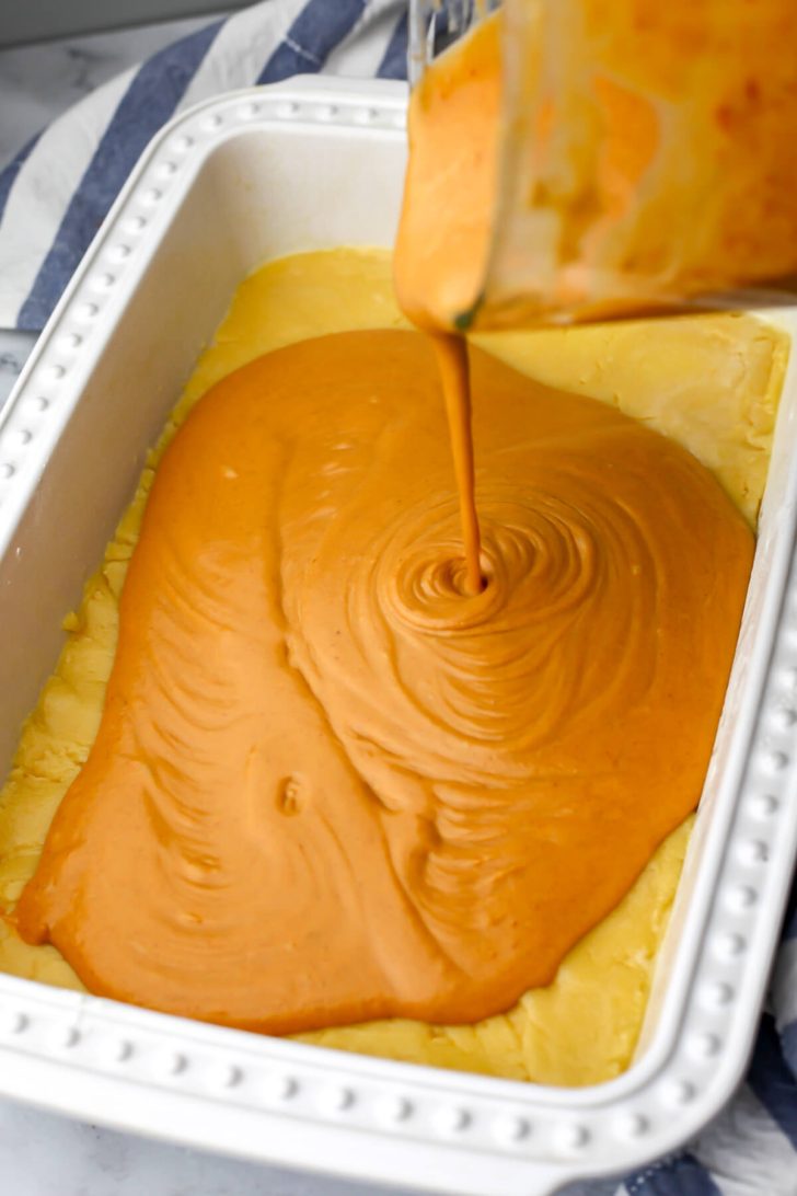 Pumpkin pie filling being poured over the first layer of the pumpkin pie cake.
