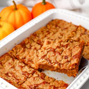 A vegan pumpkin pie cake made with cake mix and pumpkin pie filling in a white baking dish with small pumpkins behind it.