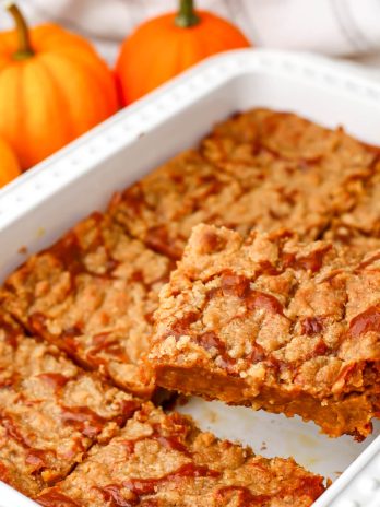 A vegan pumpkin pie cake made with cake mix and pumpkin pie filling in a white baking dish with small pumpkins behind it.