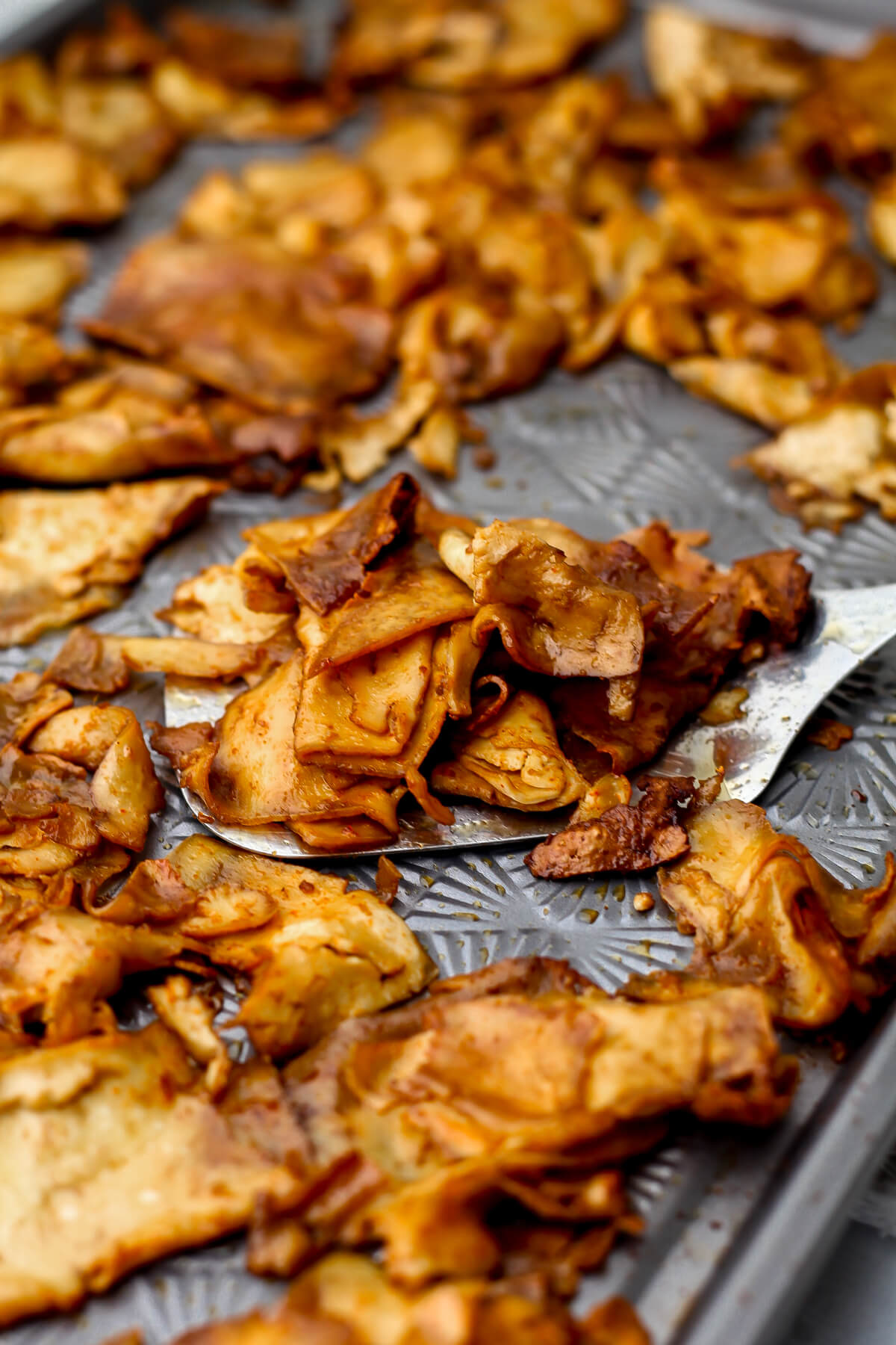A close up of tofu deli meat cooking on a sheet pan with a spatula scooping some up.