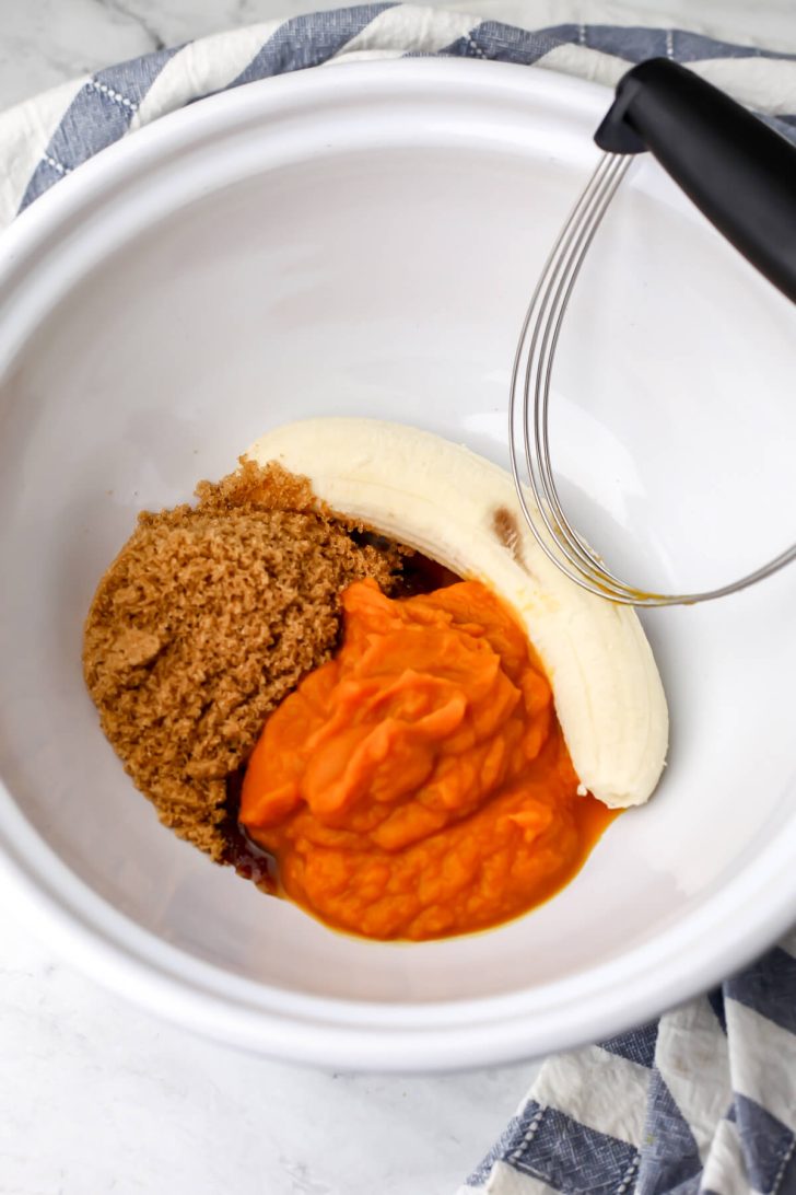 A white bowl with a banana, pumpkin puree, and brown sugar.