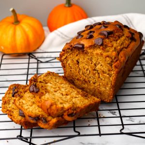 A loaf of vegan banana pumpkin bread with chocolate chips on top with some slices cut off.