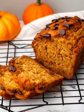 A loaf of vegan banana pumpkin bread with chocolate chips on top with some slices cut off.
