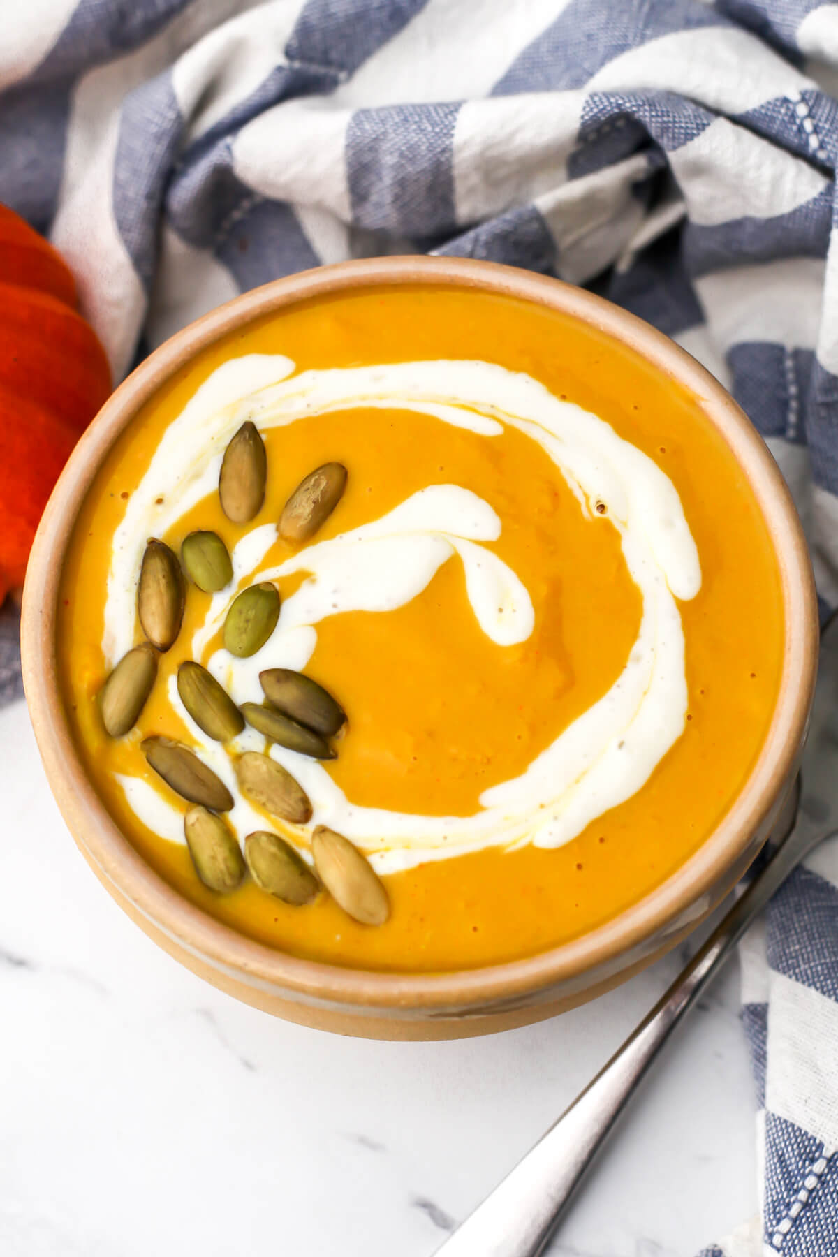 A bow of pumpkin white bean soup with a small pumpkin on the side and and blue and white tea towel.