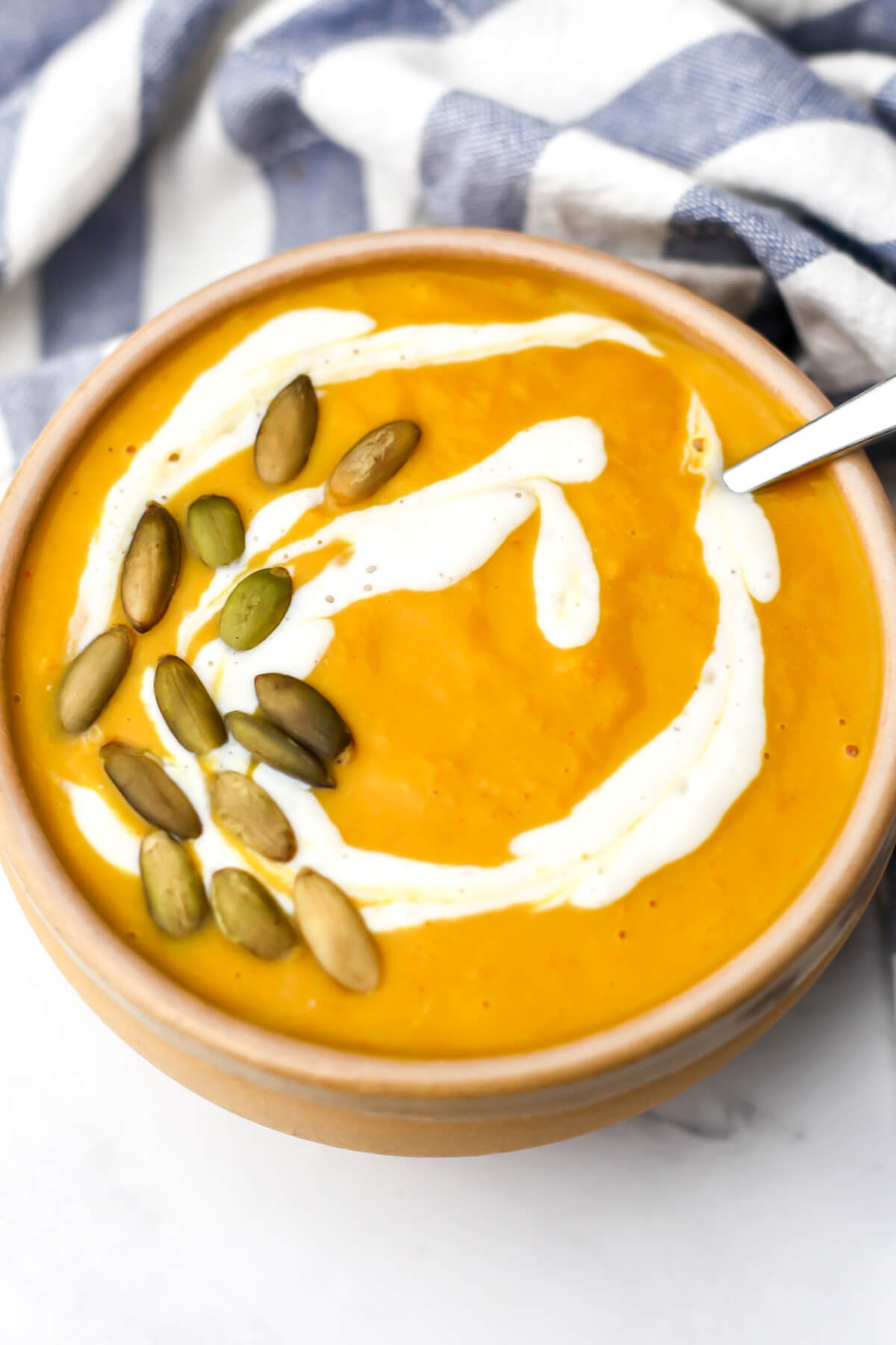 A top view of a bowl of pumpkin white bean soup with pumpkin seeds and a swirl of sour cream on top.