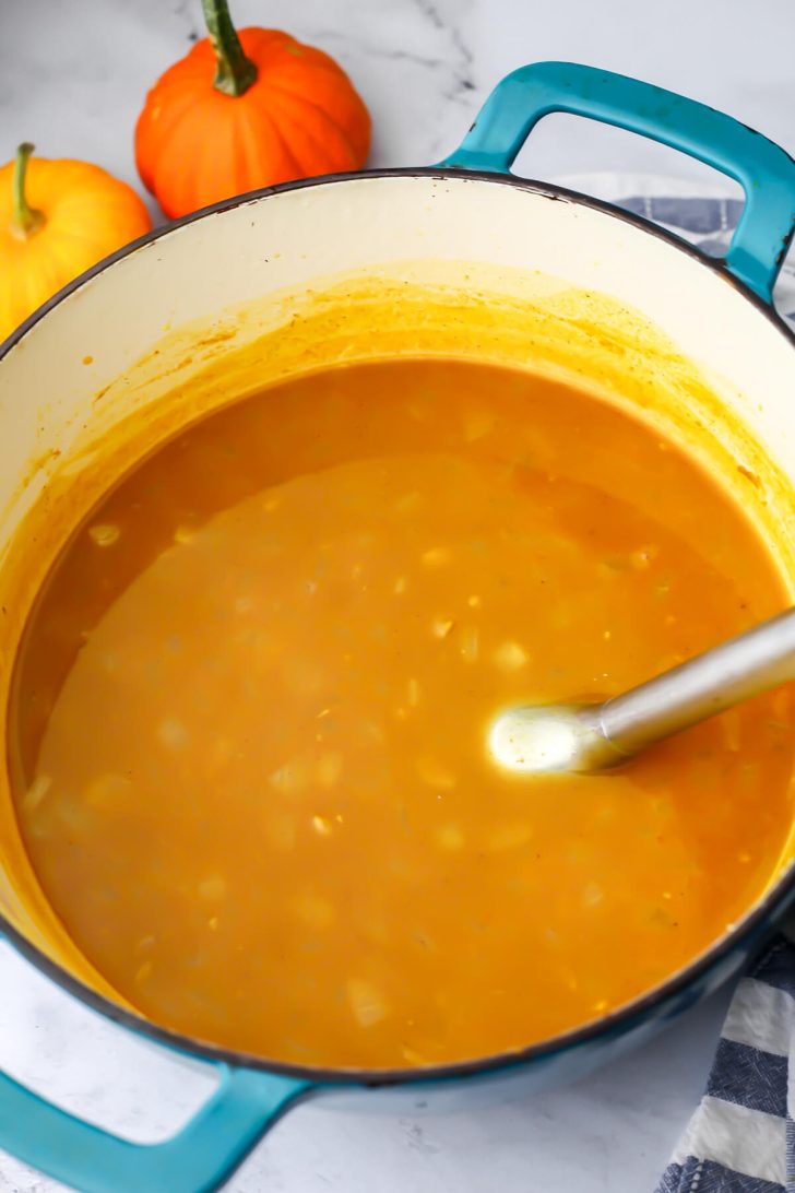 Vegan pumpkin white bean soup in a pot before it has been pureed with an immersion blender in it.