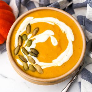 A bowl of pumpkin white bean soup with pumpkin seeds and sour cream swirled on top,