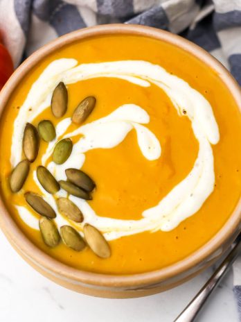 A bowl of pumpkin white bean soup with pumpkin seeds and sour cream swirled on top,