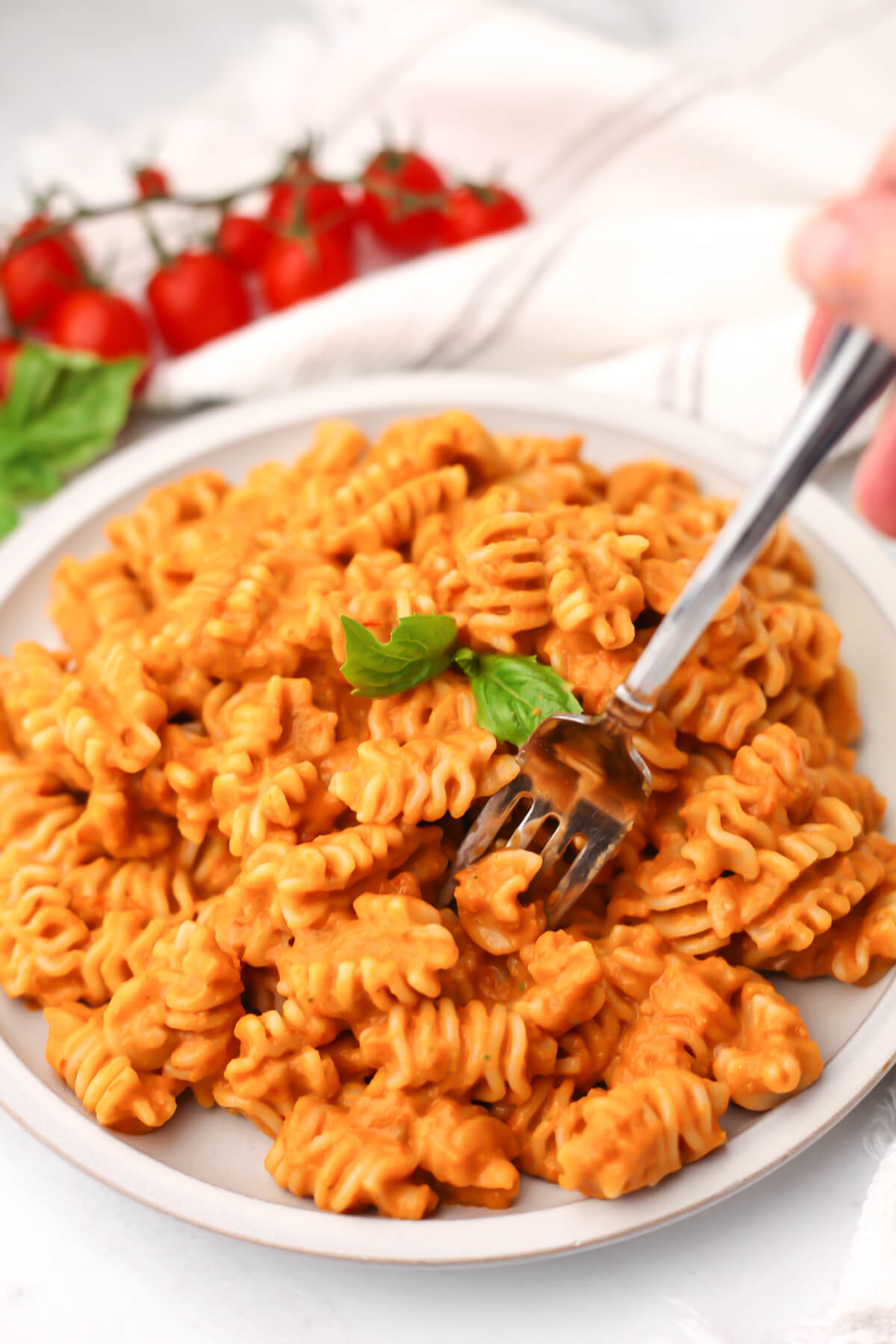 Someone sticking a fork into a plate full of creamy roasted vegetable pasta.