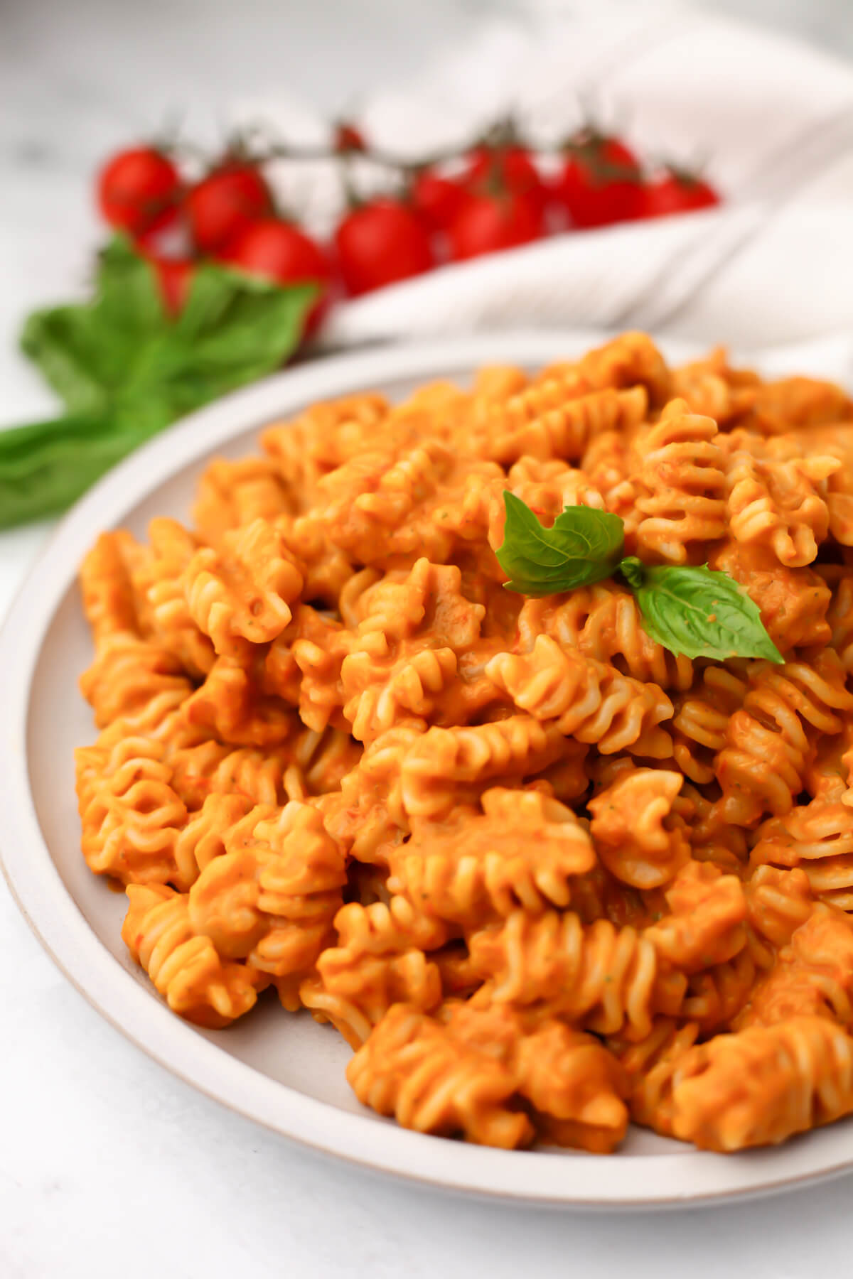 A plate full of creamy roasted vegetable pasta sauce mixed with pasta with fresh basil on top.