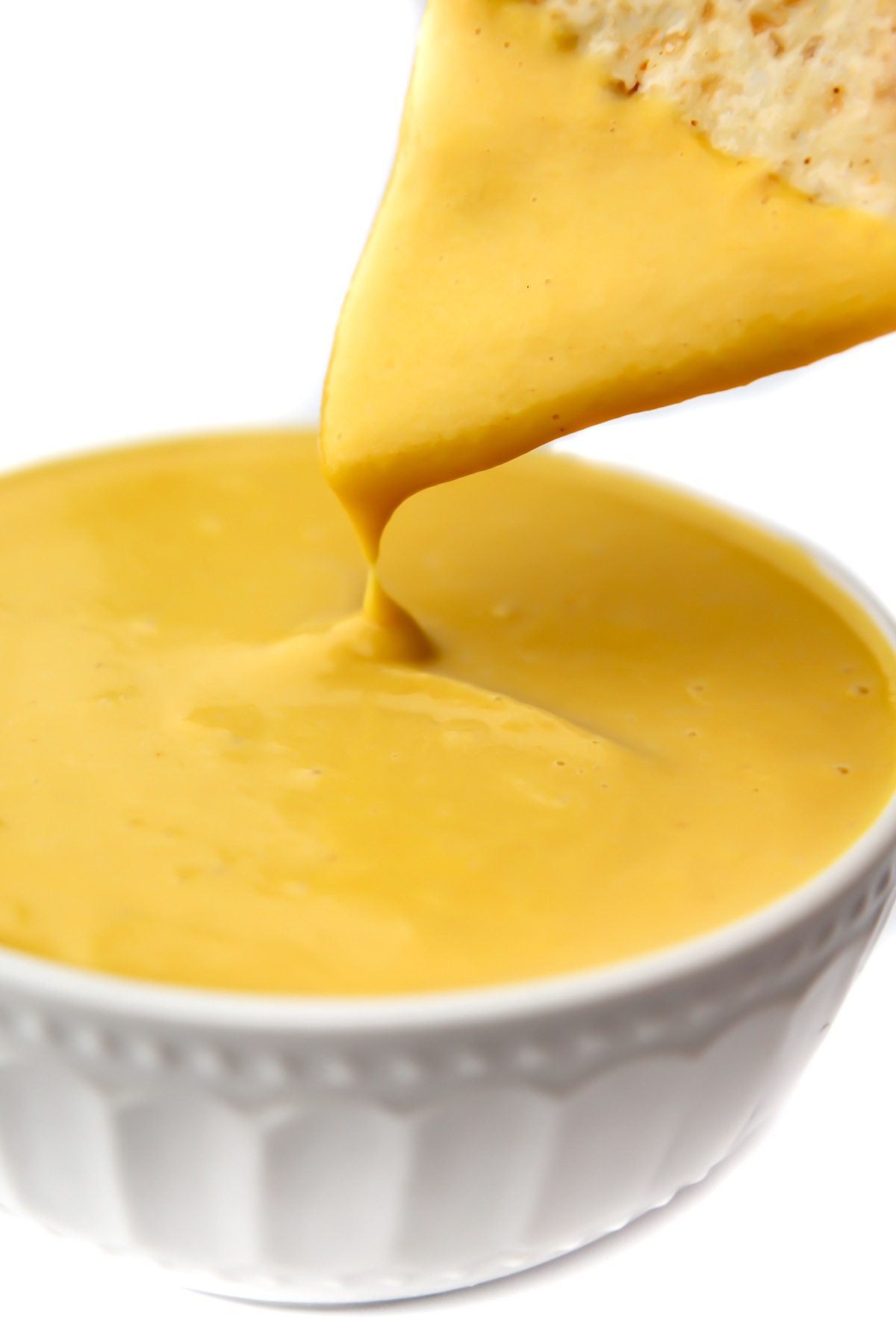 A vegan cheese sauce made from vegetables in a white bowl with a chip being dipped into it.