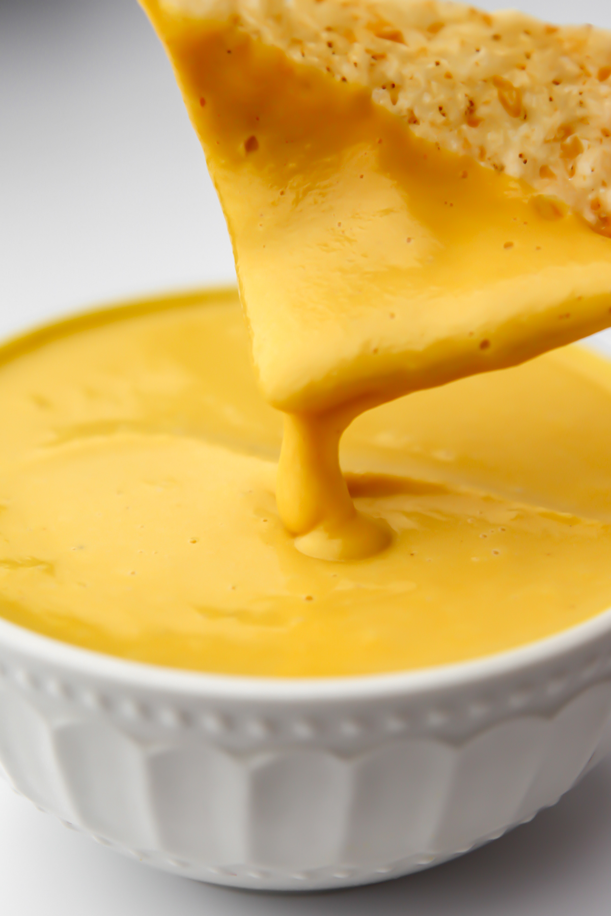 Dipping a chip in veggie cheese sauce made with squash and cashews.