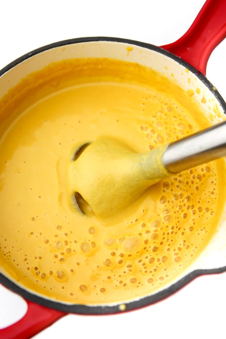 An immersion blender mixing the veggie cheese sauce in a saucepan.
