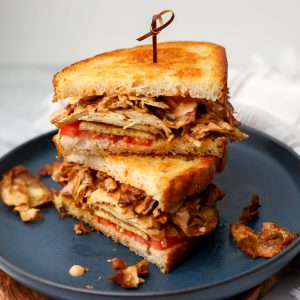 A grilled tofu sandwich made with shaved tofu on a blue plate.