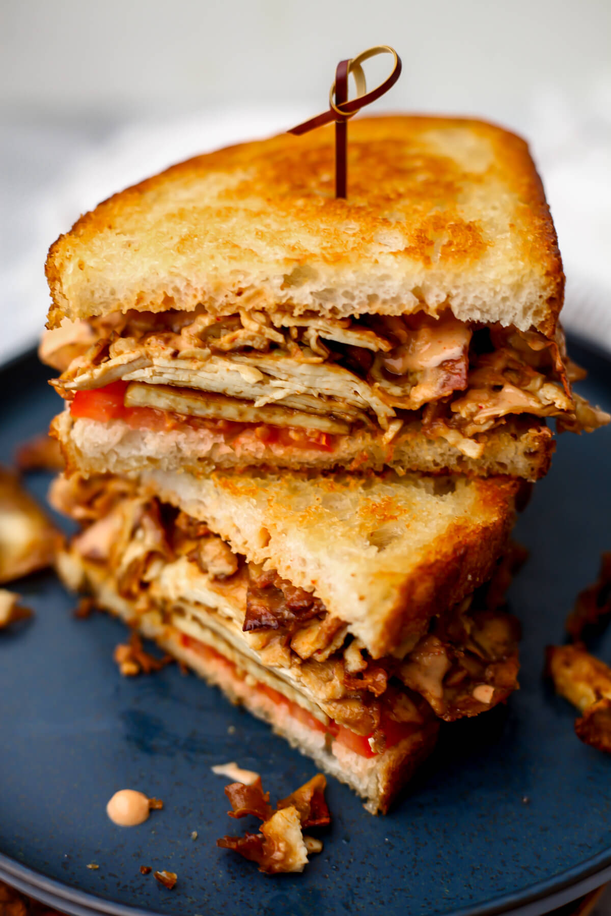 A grilled tofu sandwich cut in half and stacked on a blue plate.