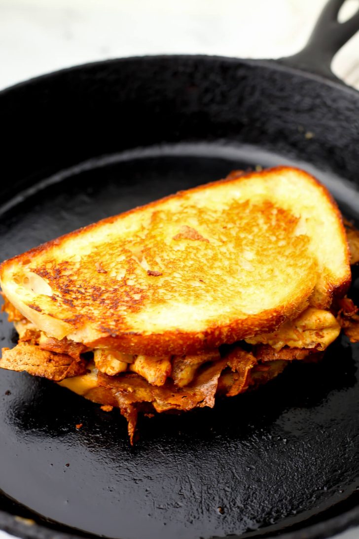 A grilled tofu sandwich cooking on an iron skillet.