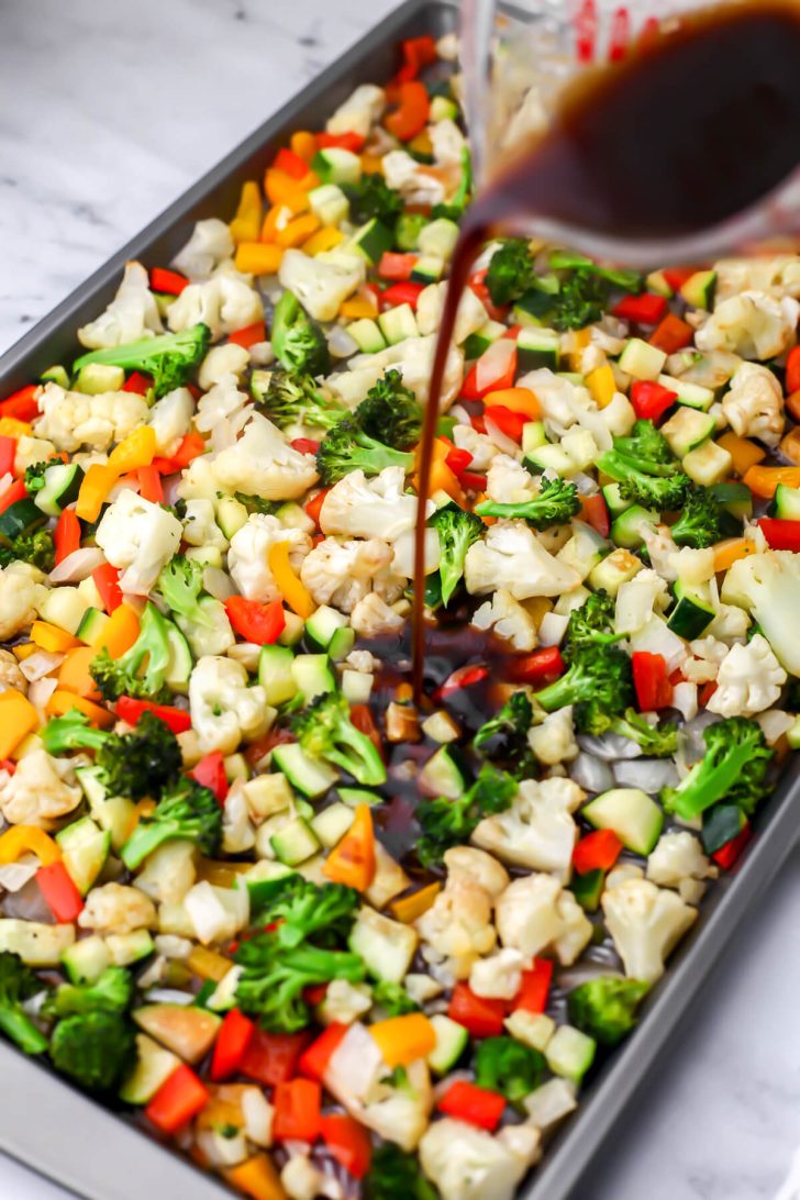 Pouring the balsamic dressing over the roasted vegetables.