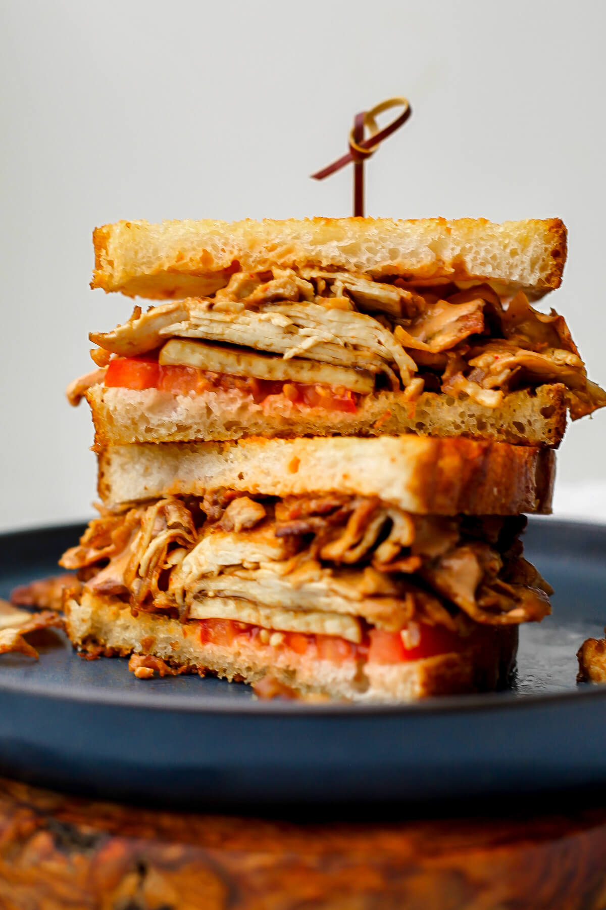 A shaved tofu sandwich cut in half and stacked on a blue plate.