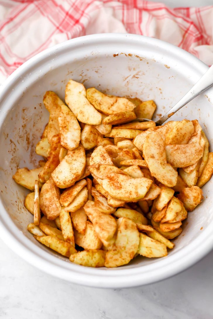 Sliced apples dusted with cornstarch, sugar, and cinnamon to make a vegan Dutch apple pie.