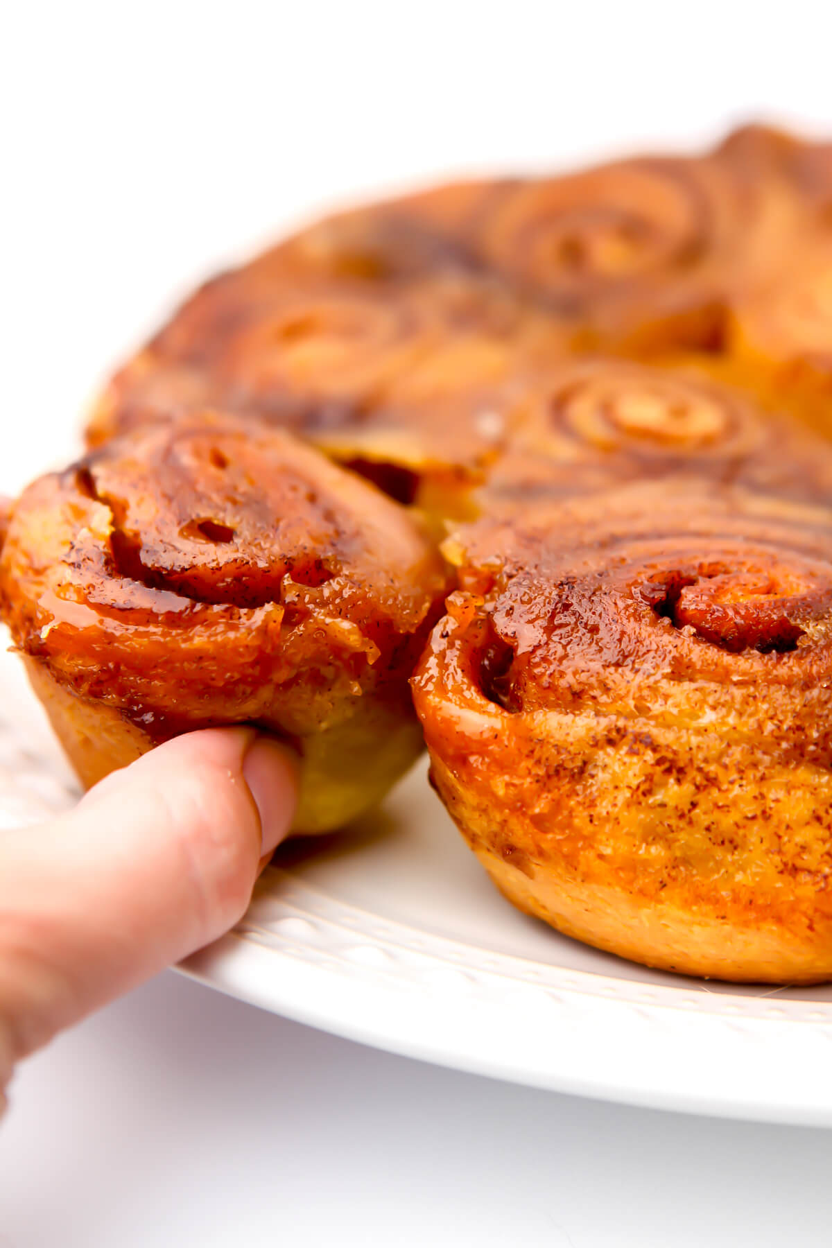 A plate of vegan sticky buns with someone taking one off the plate.