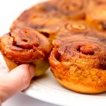 A close up of a plate of vegan sticky buns with someone taking one off the plate.
