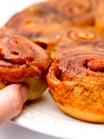 A close up of a plate of vegan sticky buns with someone taking one off the plate.