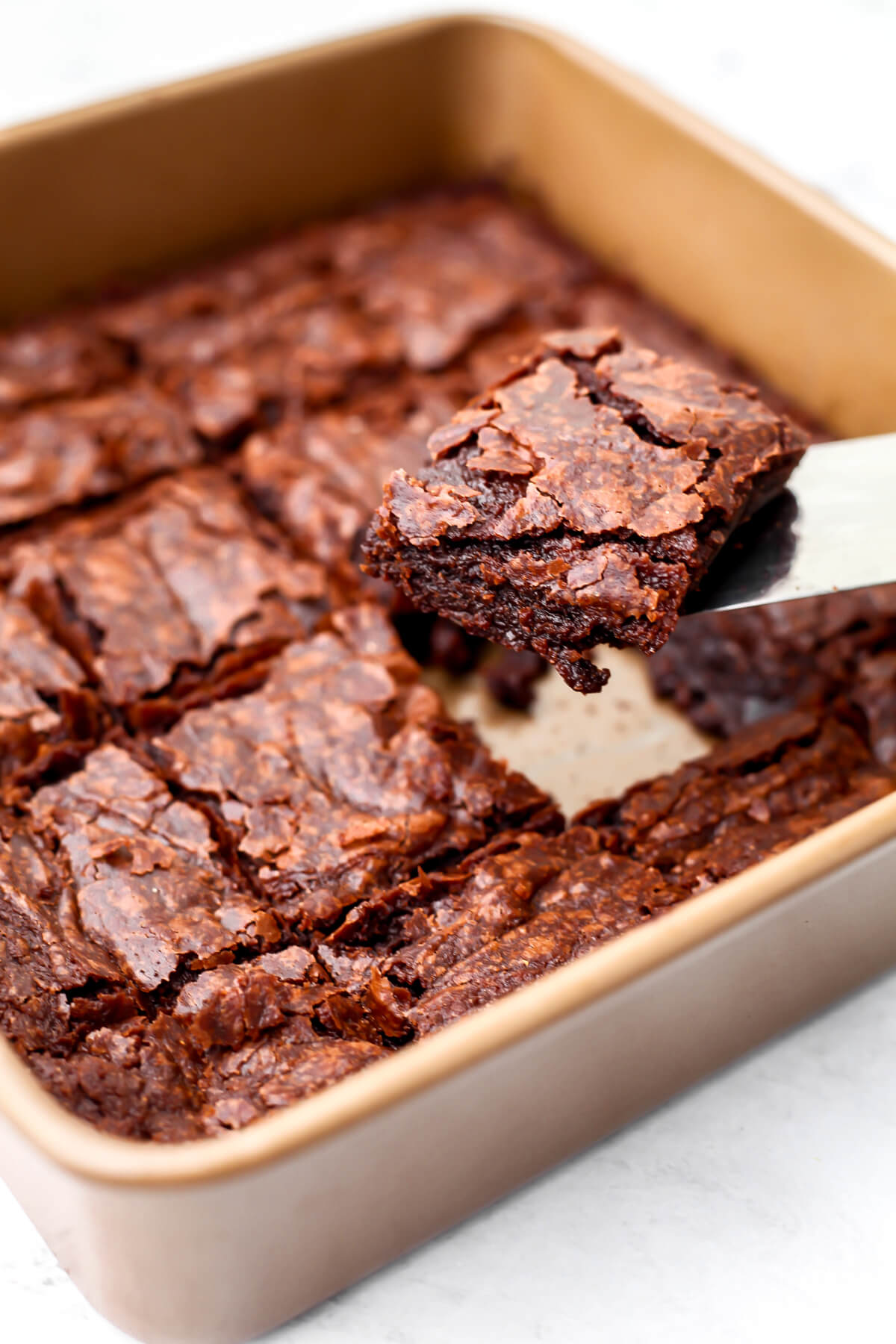 Someone taking a brownie out of a pan of brownies cut into squares.