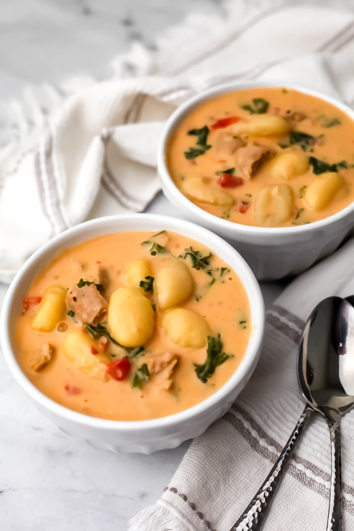 Two bowls of creamy vegan gnocchi soup with sausage and kale.