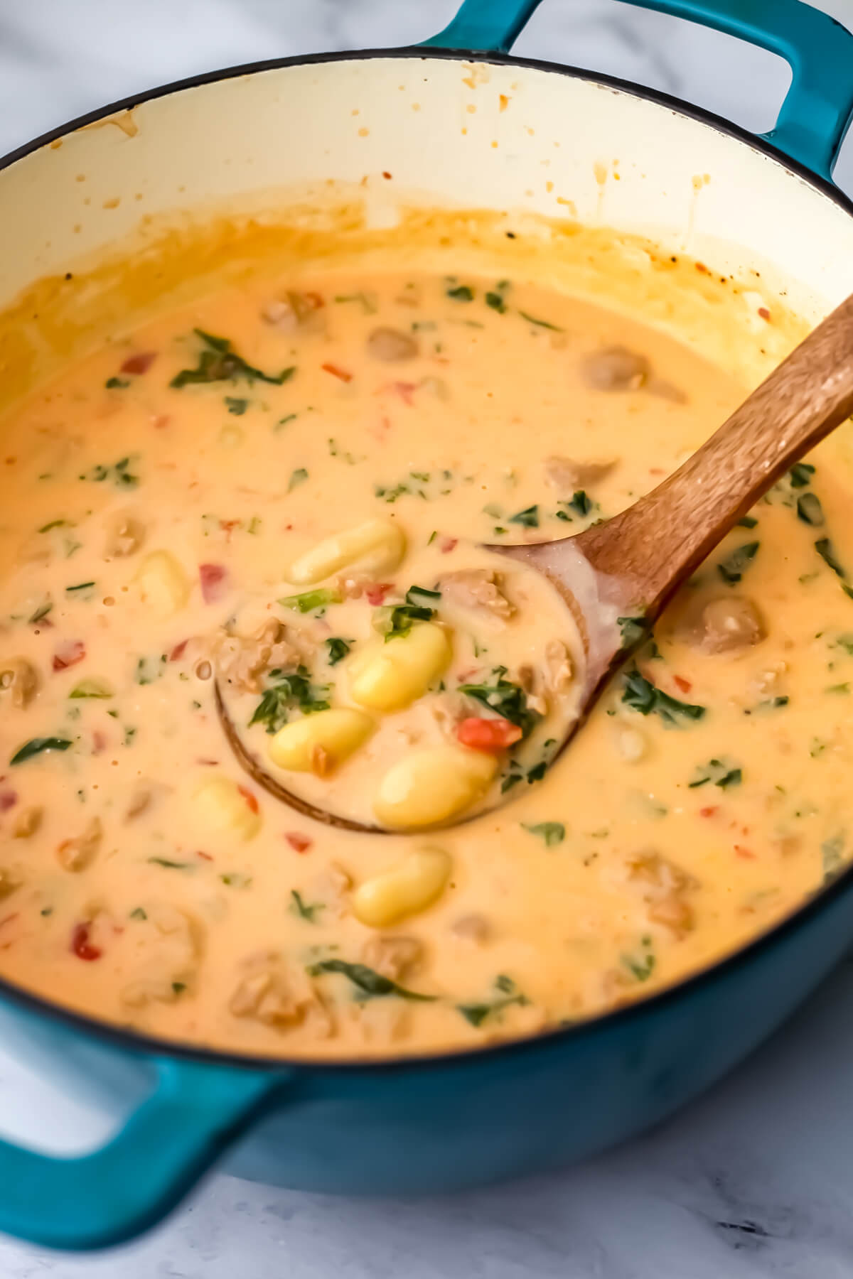 A large blue soup pot filled with creamy vegan gnocchi soup with spinach and kale.