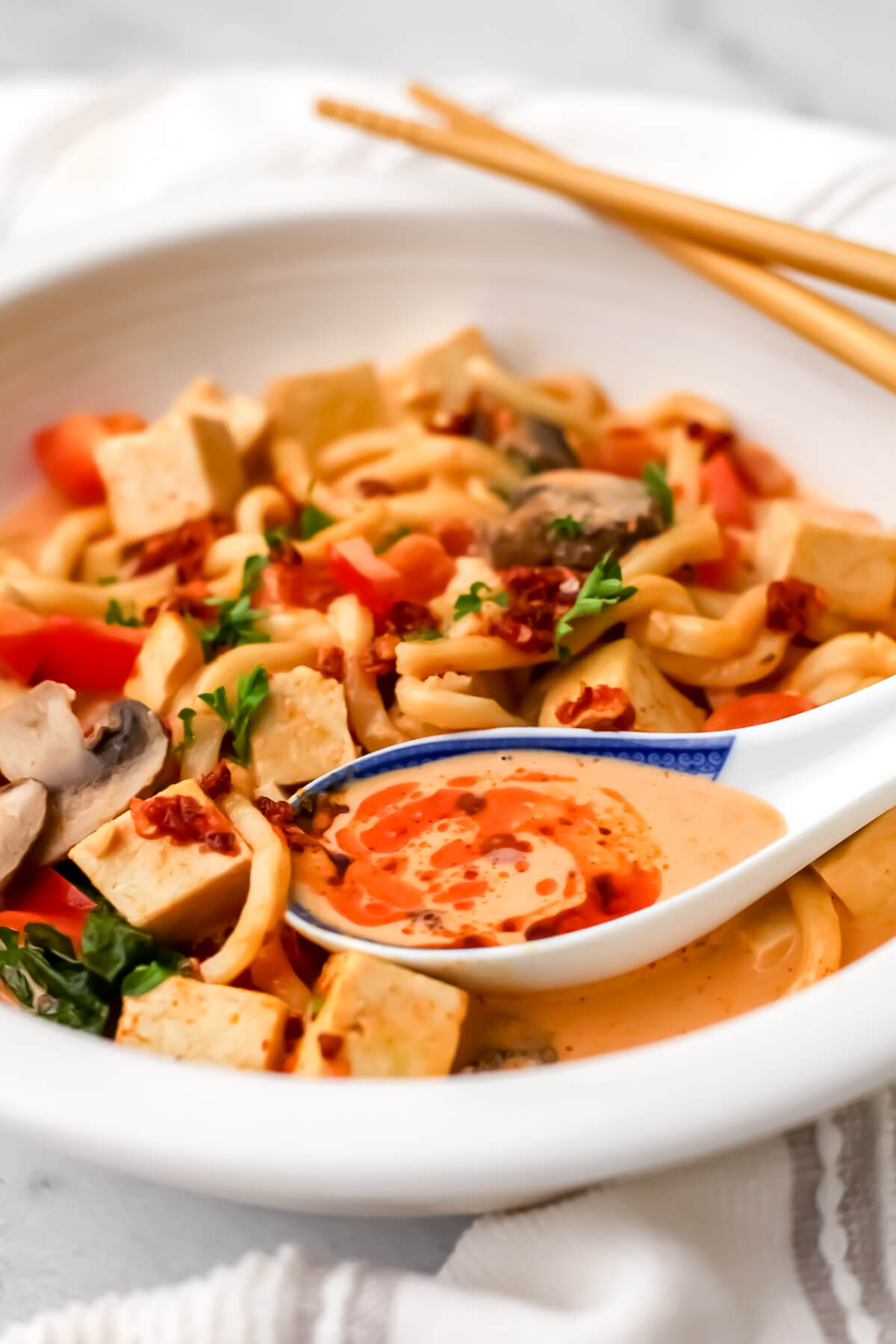 A bowl of red curry noodles in a coconut curry broth topped with herbs and chili oil.