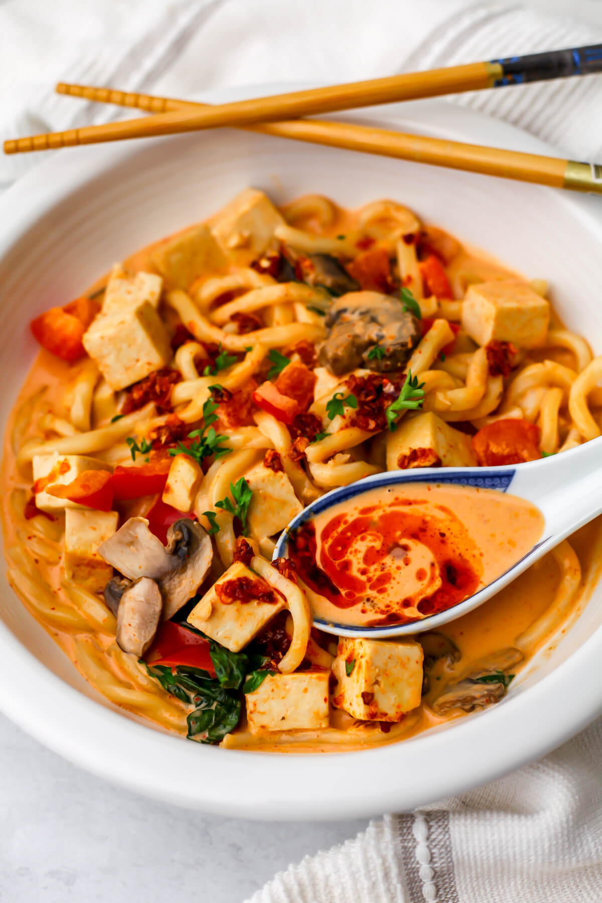 Thai red curry noodles in coconut milk sauce in a white bowl with chili oil drizzled on top.