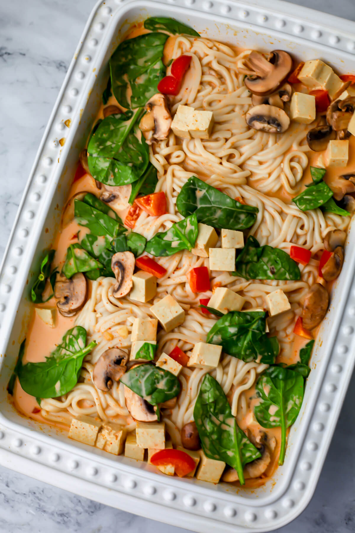 Vegetables, tofu, and noodles added to the red curry sauce in a casserole dish.