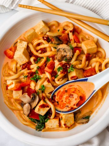 A white bowl full of noodles and tofu in a Thai red curry coconut sauce.