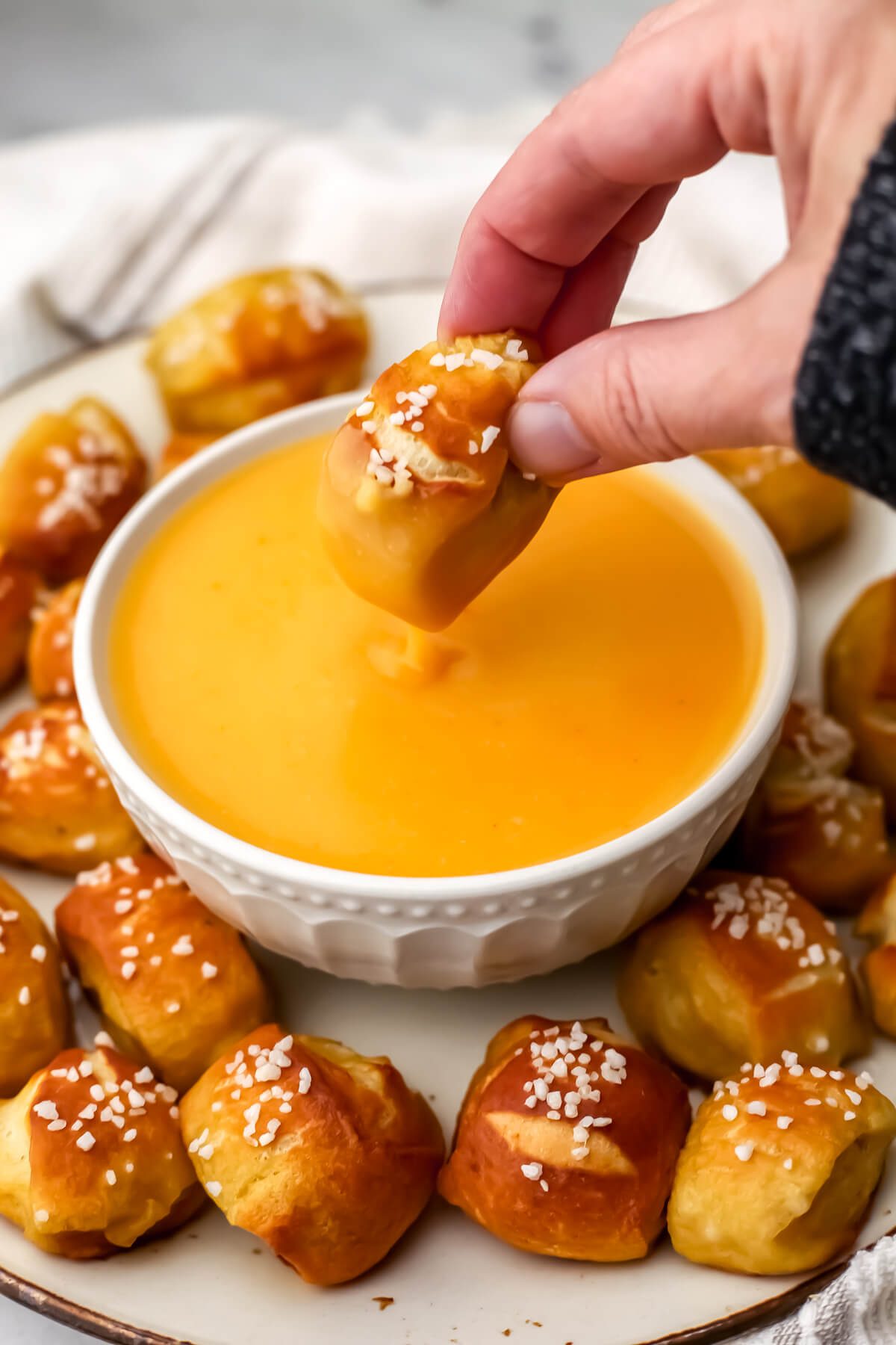 A white bowl filled with vegan beer cheese dip with someone dipping a pretzel bit into it.