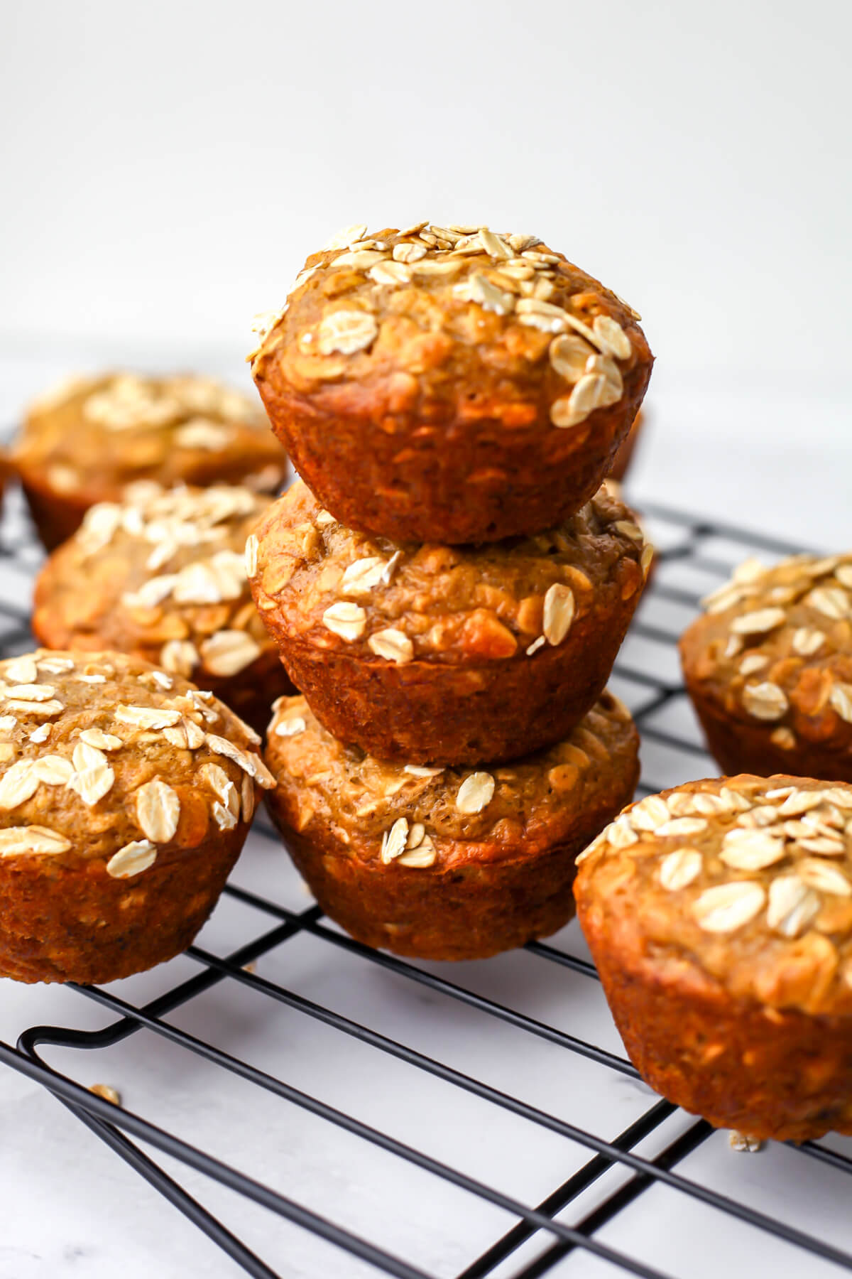 Vegan oatmeal muffins stack on top of each other on a cooling rack.