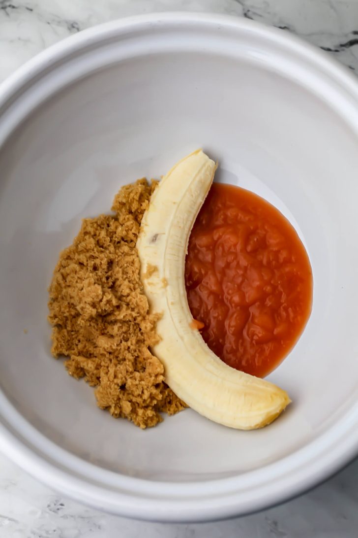 Brown sugar, applesauce and a banana in a mixing bowl.