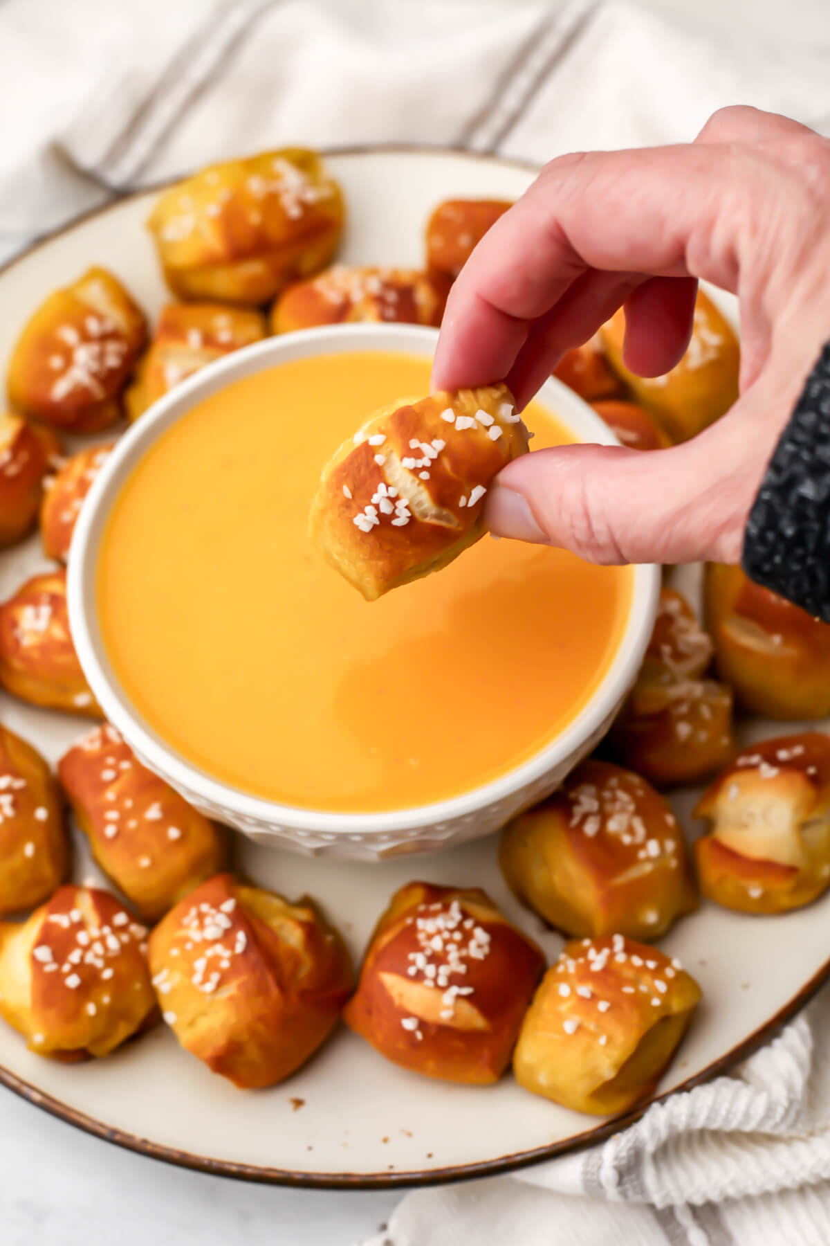 A vegan soft pretzel bite being dipped into vegan beer cheese sauce,