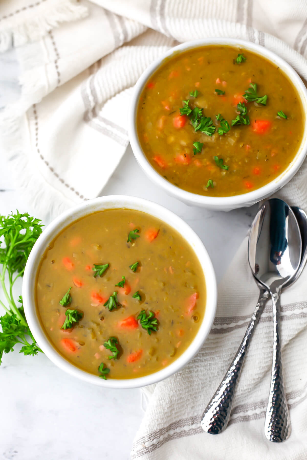 A top view of vegan split pea soup in white bowls with spoons on the side.