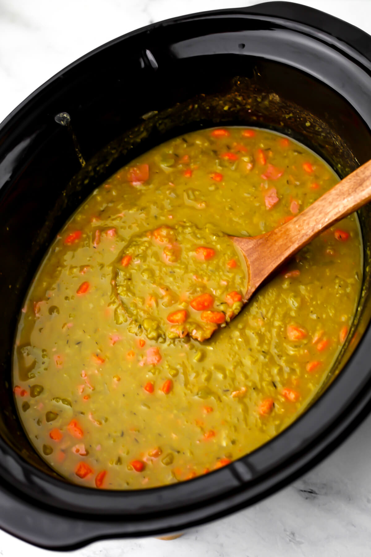 A slow cooker filled with vegan split pea soup made with carrots, celery, and bacon bits.