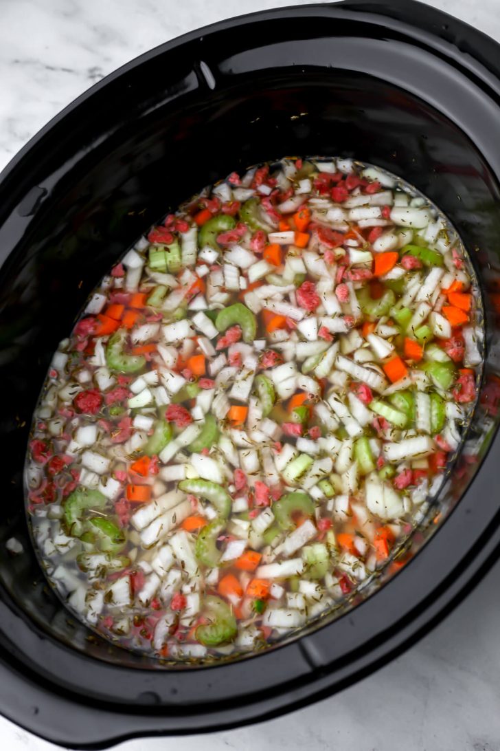 The broth added to all of the ingredients for vegan split pea soup in a slow cooker and stirred together.