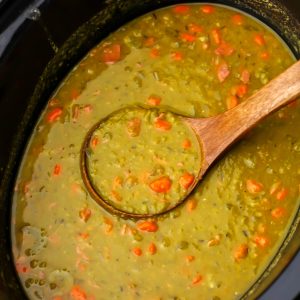 A close up of a slow cooker full of vegan split pea soup with a wooden ladle scooping some out.