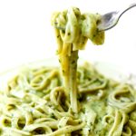 A plate filled with creamy vegan pesto sauce over pasta and a fork full of the pasta over the dish.