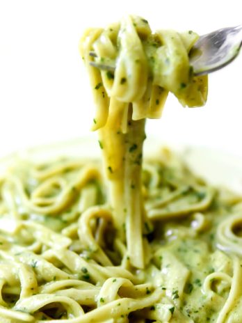 A plate filled with creamy vegan pesto sauce over pasta and a fork full of the pasta over the dish.