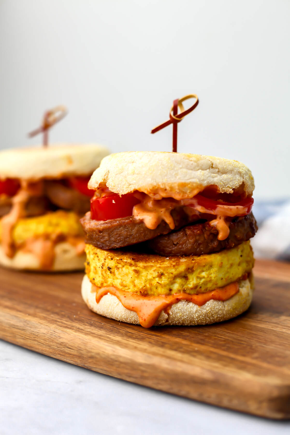 Two vegan tofu breakfast sandwiches on a wooden cutting board.