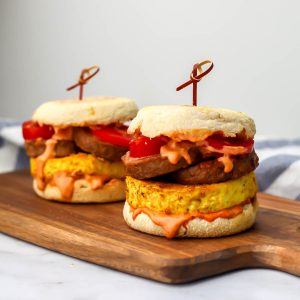Two vegan tofu breakfast sandwiches on English muffins with vegan breakfast sausage.